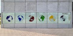 Blick auf das Hausschild mit den sechs Kontinenten – der Künstler Olaf Thaler:  Die sechs globalen Ansichten vermitteln zudem die zentrale  Achse   um die sich die Welt bei aller Vielfalt von Land und Leuten dreht. Das farbige Glas betont die Schönheit  d © 2021 SBL Neubrandenburg